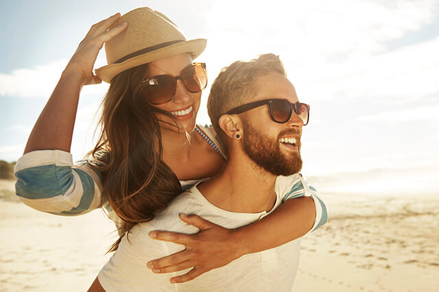 Young couple with sunglasses smiling on a beach.
