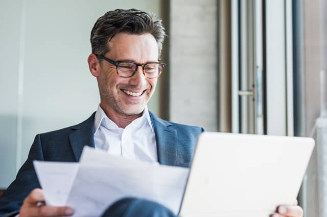 Businessman with glasses smiling and using a laptop.