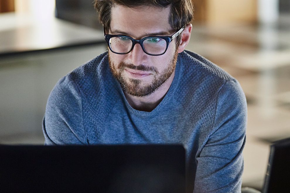 Young man with glasses looking at a computer.