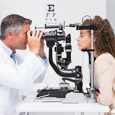 An eye doctor performs an eye exam on a young woman