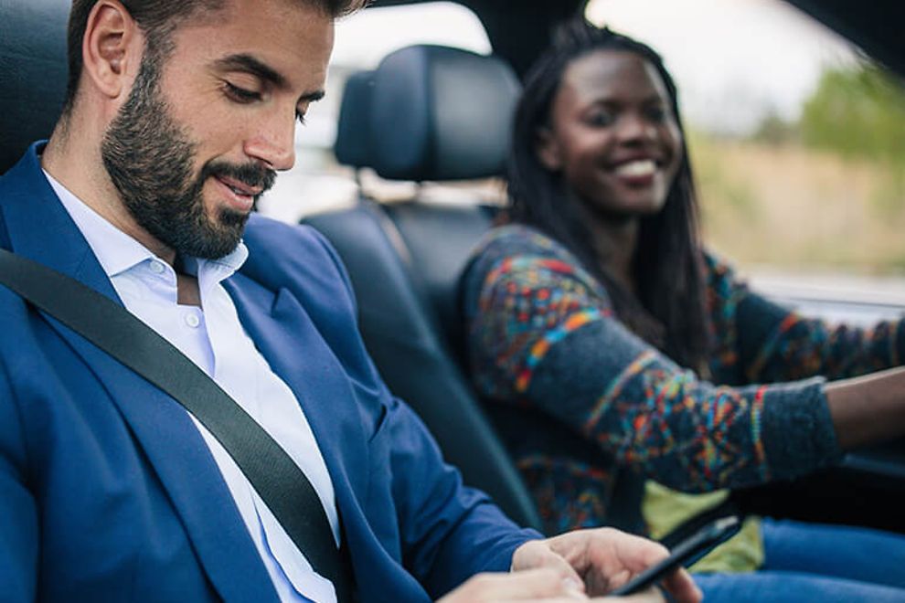 Businessman uses an app in a car while a woman drives